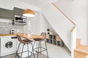 Uma cozinha moderna com máquina de lavar embutida, dois bancos altos e uma escada de madeira.