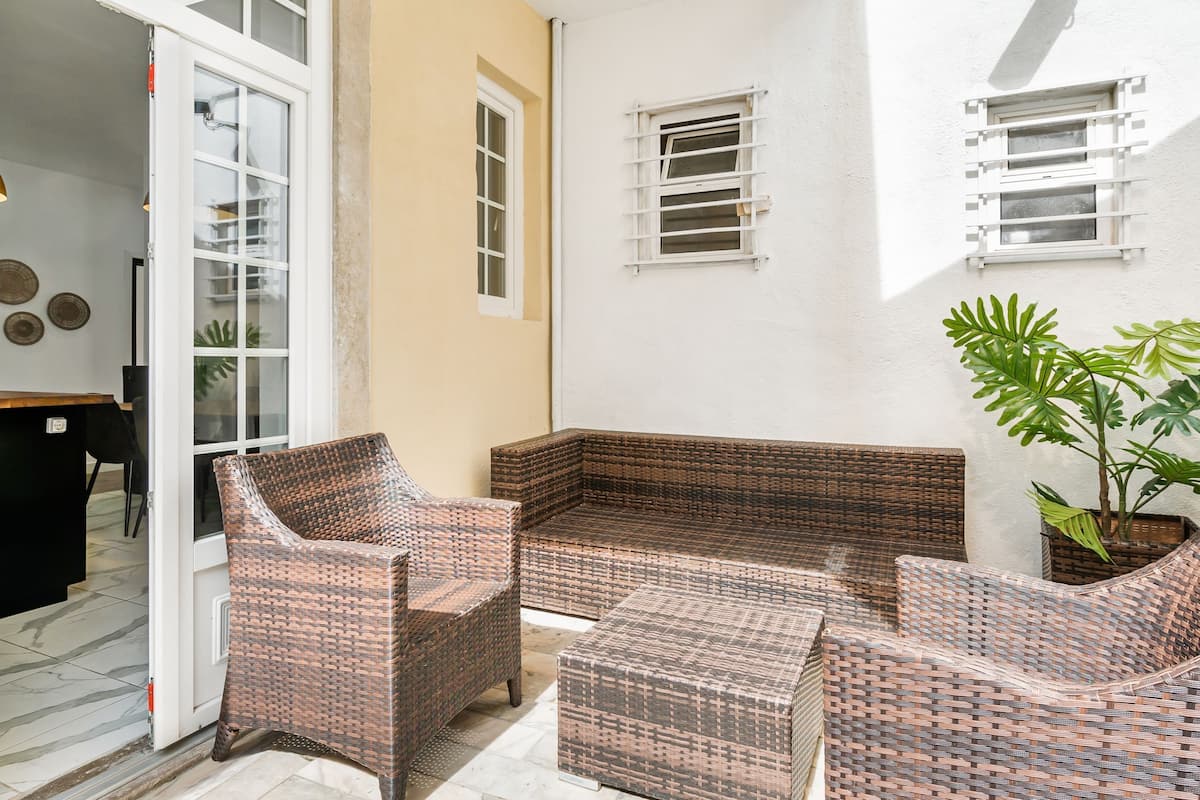Un espace patio aménagé avec des meubles en osier, une plante en pot et un mur blanc agrémenté de fenêtres.