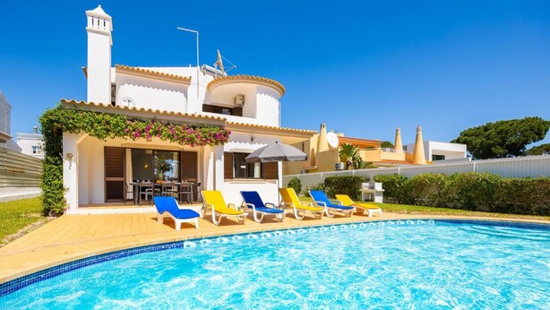 A swimming pool with sun loungers, a covered seating area, and a building with a white facade and a chimney. - Villa Cavaco - Four Bedroom Villa, Sleeps 8 (Quarteira)