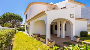 A white building with arches and a tiled roof, surrounded by a well-maintained garden and a clear sky. - Villa Cavaco - Four Bedroom Villa, Sleeps 8 (Quarteira)