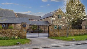A stone building with a gated entrance, a grassy lawn, and a tree with white blossoms. - The Old Stables (Northampton)