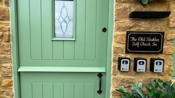 Una puerta verde con una ventana, un cartel que dice 'welcome', un cartel que indica 'The Old Stables Self Check In' y tres llaves numeradas.