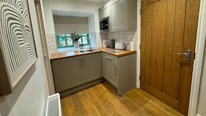 A compact kitchen with grey cabinets, a wooden countertop, a microwave, and a wooden door. - The Old Stables (Northampton)