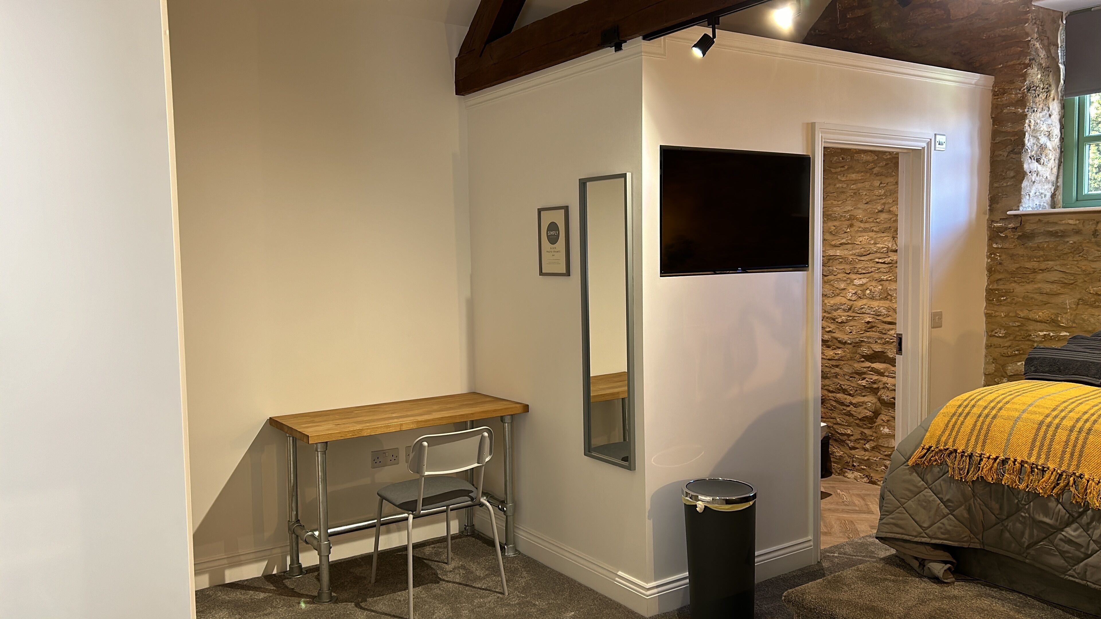 A bedroom with a bed, a bedside table, a chair, a mirror, and a TV.