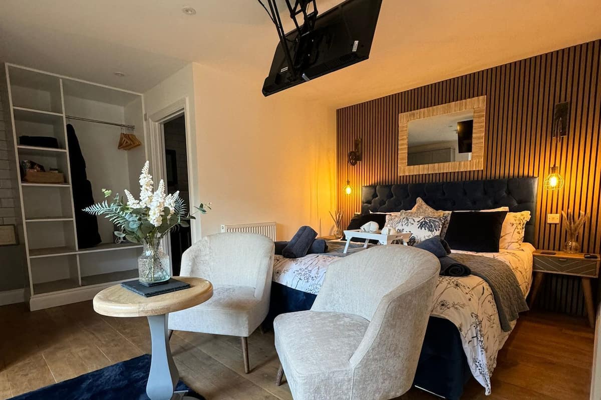 A modern bedroom with a bed, two armchairs, a small round table, and a large mirror.