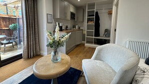 A modern living room with a sofa, a coffee table, and a vase with flowers. There is a kitchen area with cabinets and a microwave. - The Old Stables (Northampton)