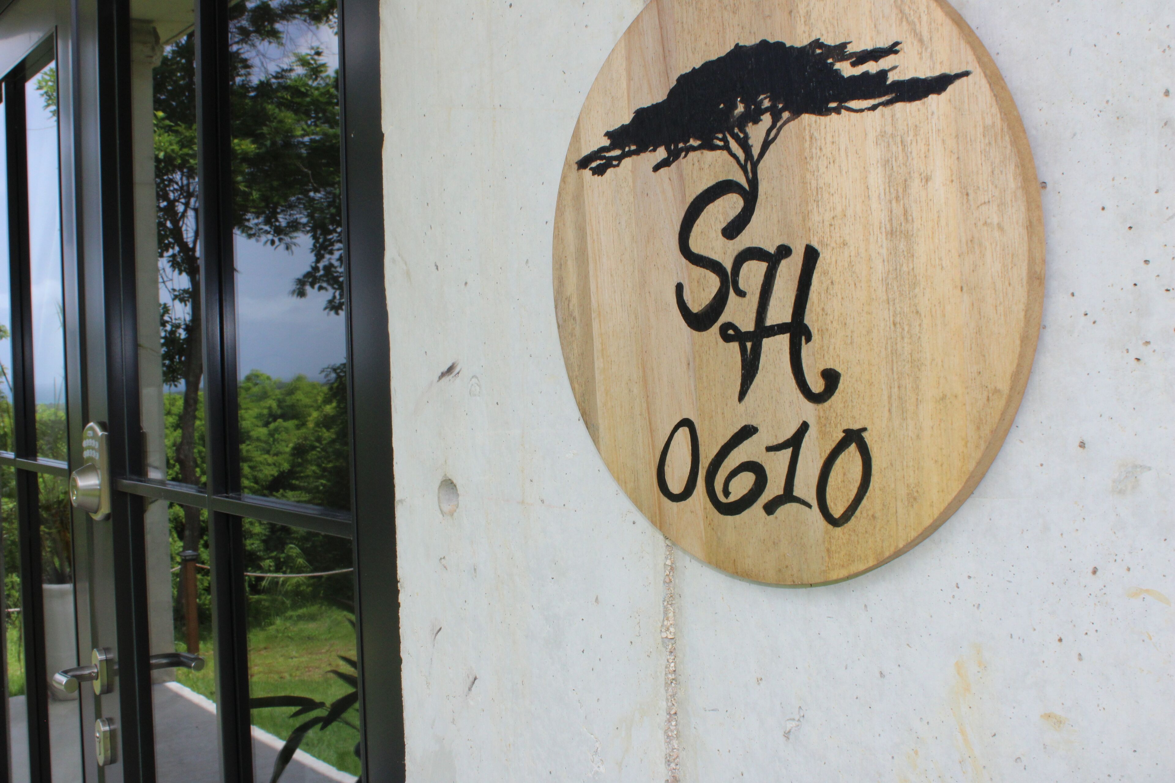 A wooden sign with a tree silhouette and the letters "SH" and the number "0610" on a white wall.