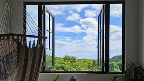 Une pièce dotée d’une grande fenêtre, d’un fauteuil suspendu et de deux plantes en pot.