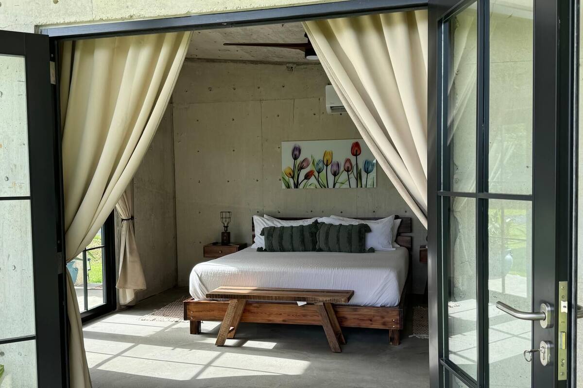 Une chambre avec un lit en bois, un banc et un tableau représentant des fleurs accroché au mur.
