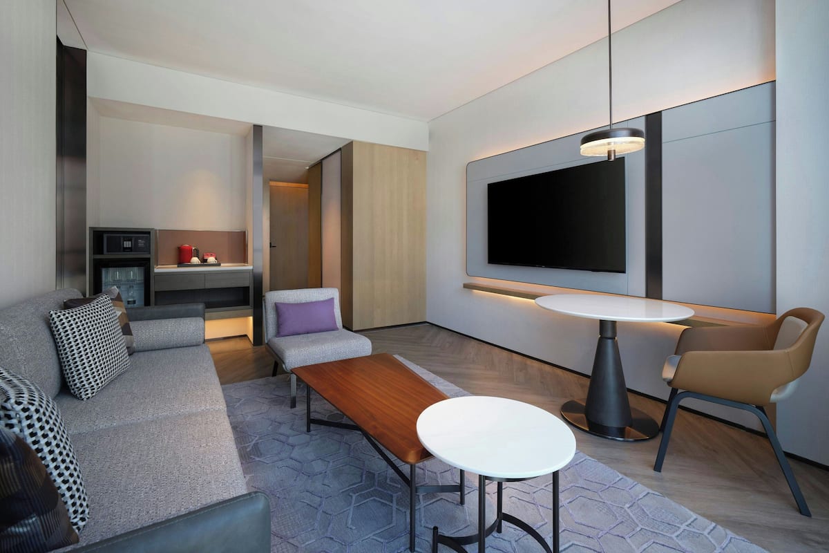 A modern living area with a sofa, a coffee table, a TV mounted on the wall, and a small kitchen area.