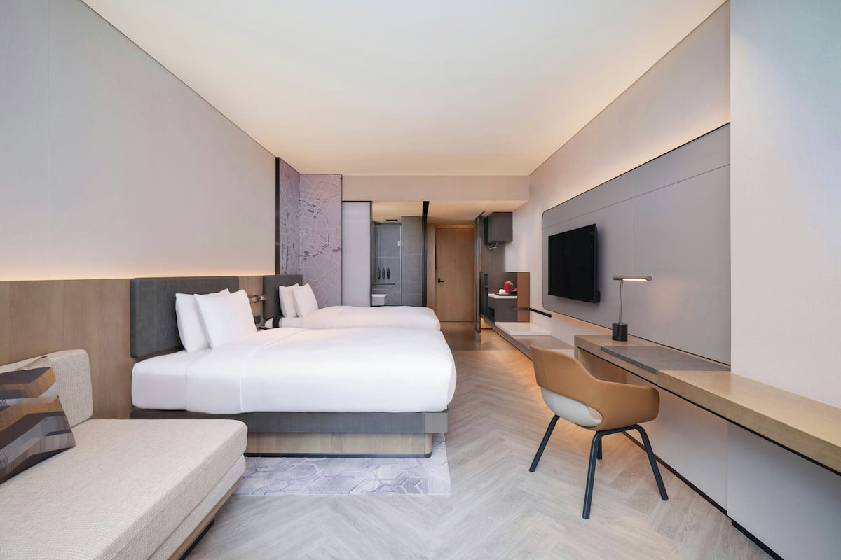 A modern hotel room with a large bed, a desk, a chair, and a TV.