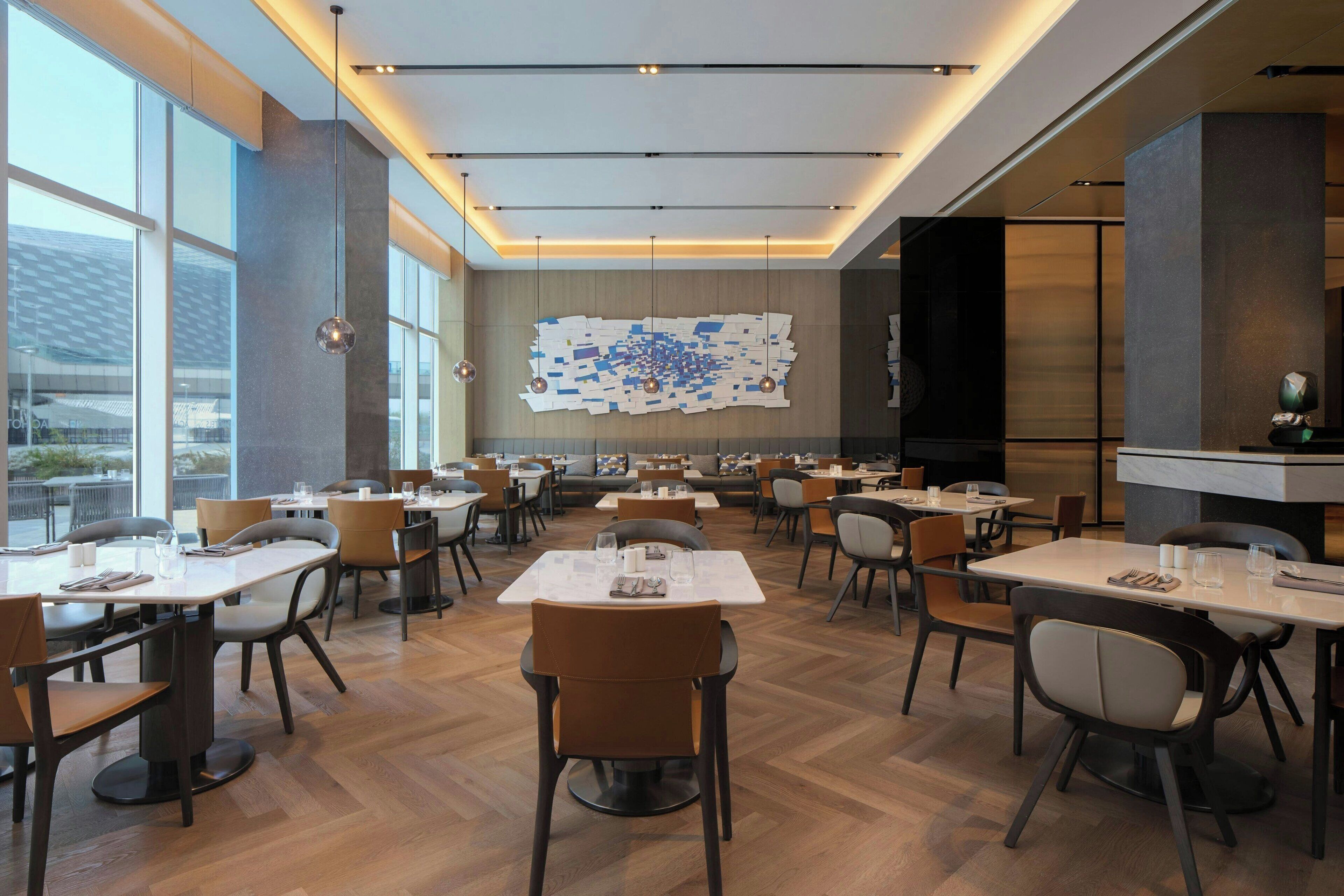 A modern dining area with multiple tables and chairs, large windows, and a unique wall art installation.