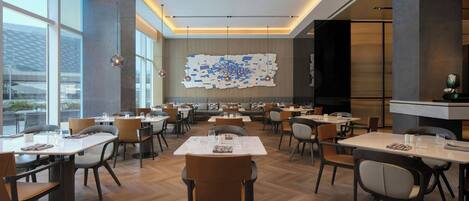 A modern dining area with multiple tables and chairs, large windows, and a unique wall art installation.