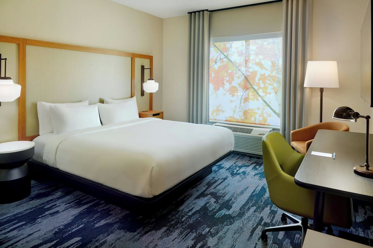 Una habitación de hotel con una cama grande, un escritorio, una silla y un ventanal con cortinas.