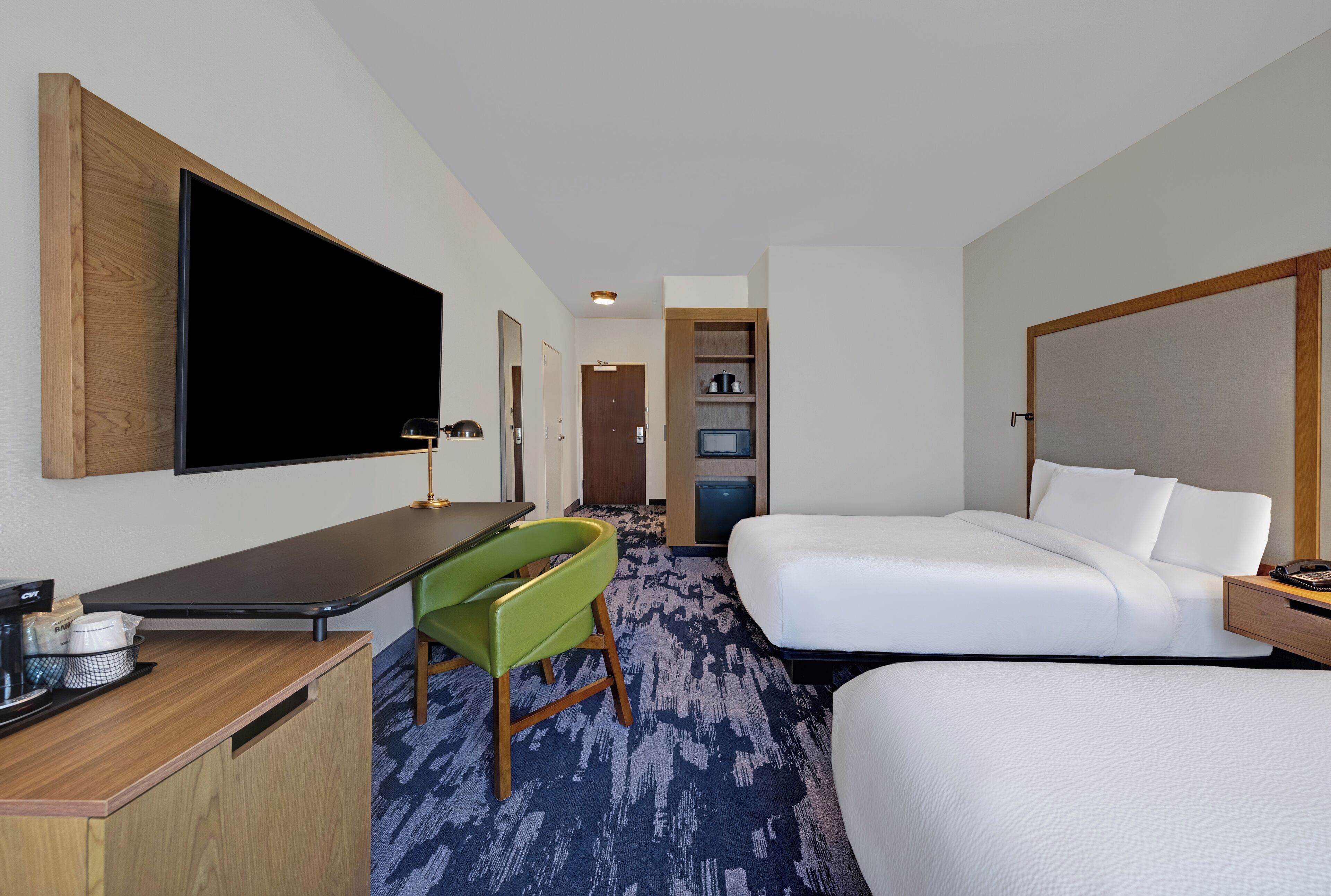 Une chambre d’hôtel avec un grand lit, un bureau doté d’un téléviseur à écran plat, un fauteuil vert et une petite kitchenette.