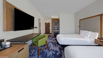 Une chambre d’hôtel avec un grand lit, un bureau doté d’un téléviseur à écran plat, un fauteuil vert et une petite kitchenette.