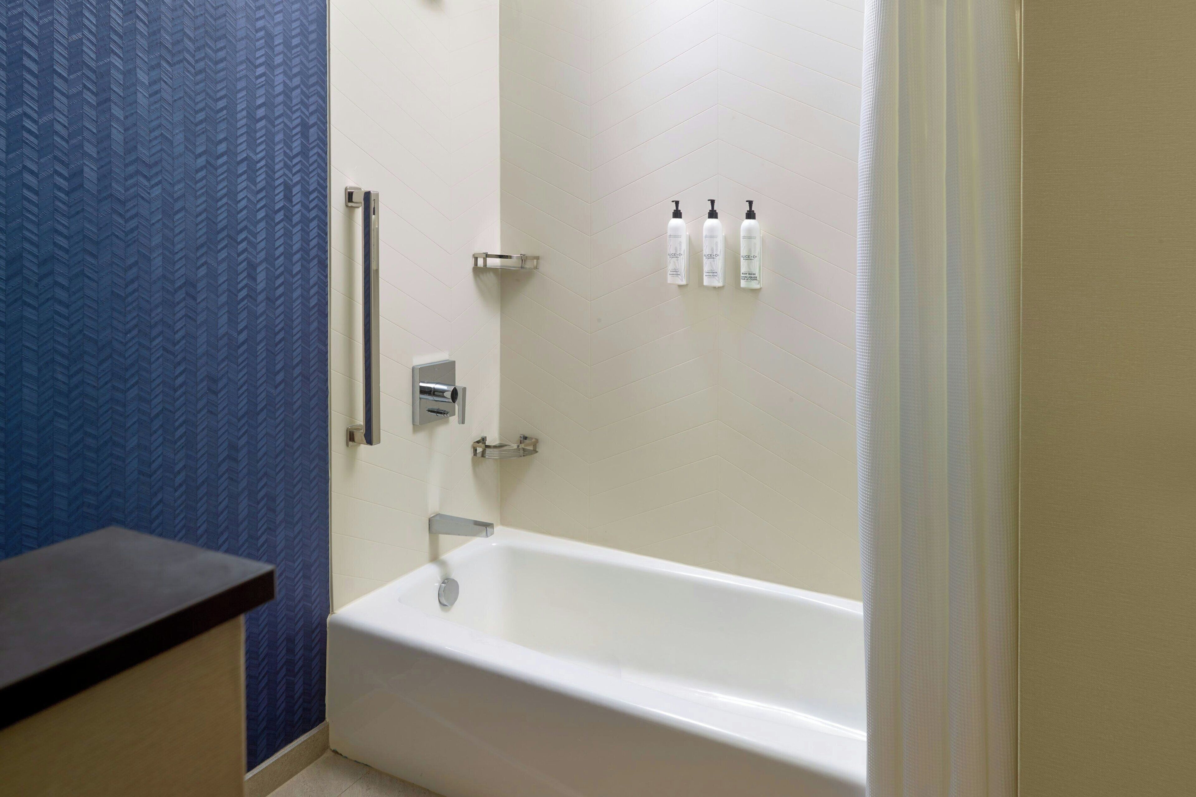 Un baño con una bañera blanca, una pared azul con textura y tres botellas de artículos de aseo en la pared.
