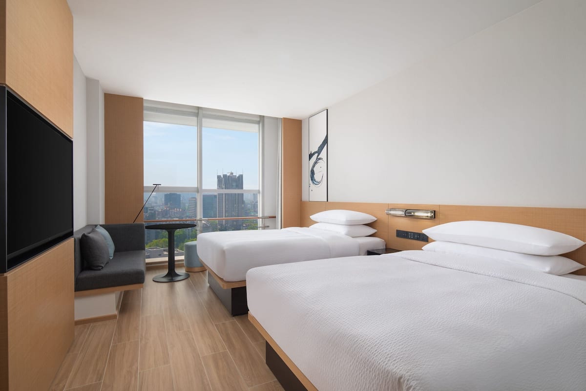 Habitación de hotel con dos camas, televisor, una mesita y vista a la ciudad.