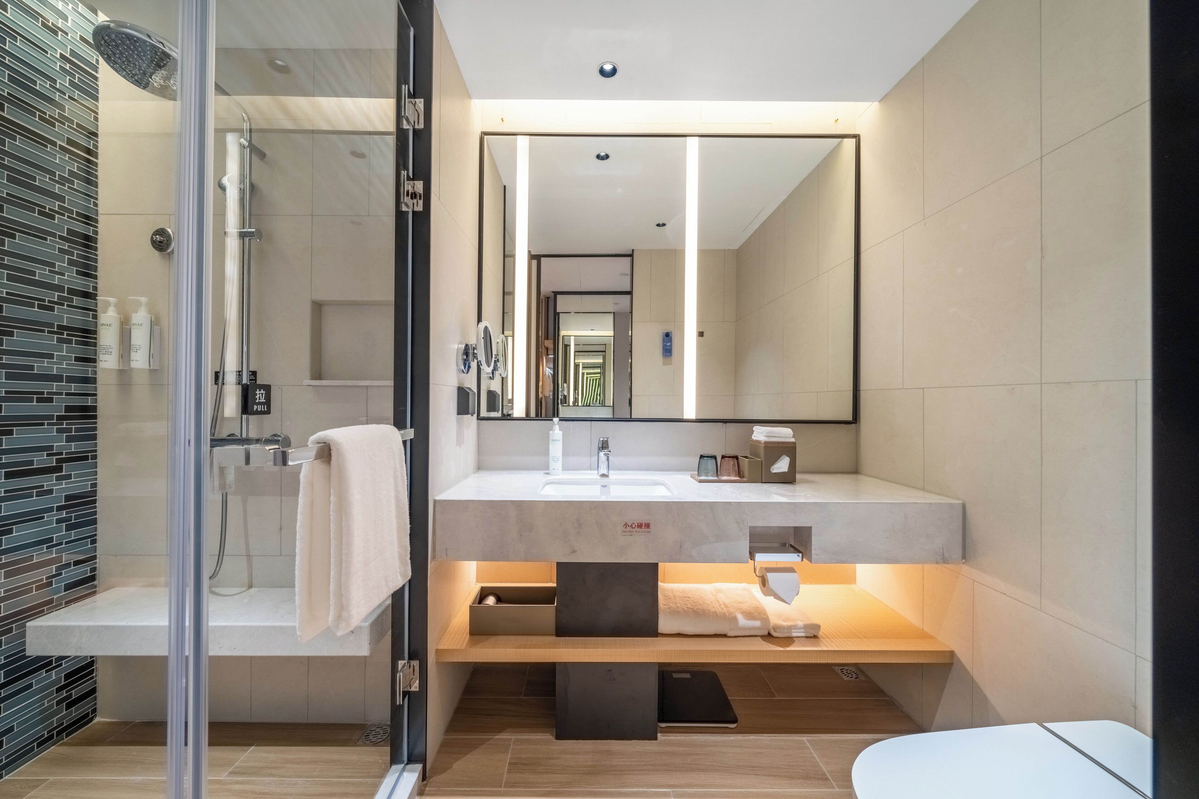 A modern bathroom with a glass-enclosed shower, a large mirror, and a vanity with a sink and towel rack.