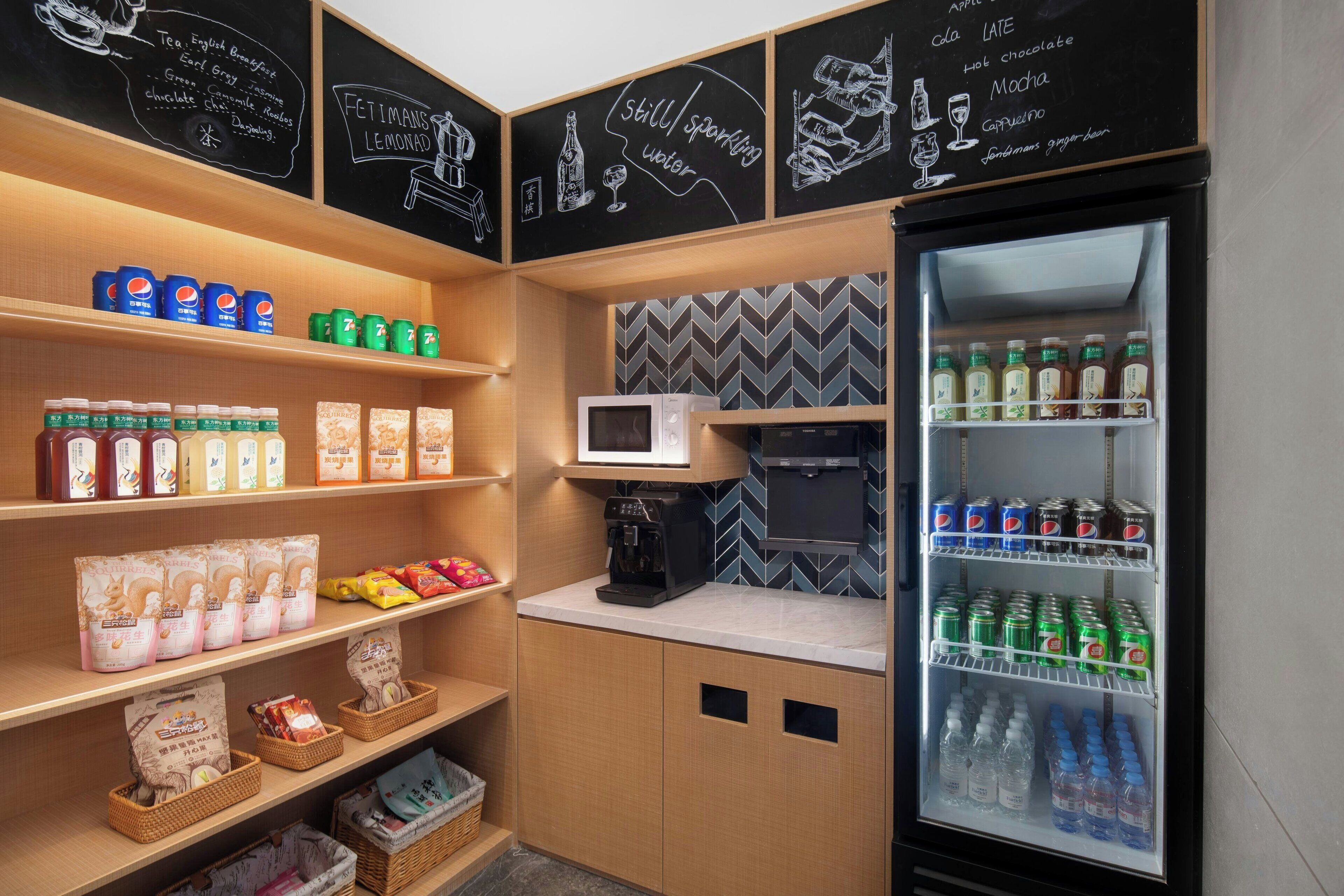 A kitchenette with a refrigerator stocked with beverages, a microwave, and shelves with condiments and snacks.