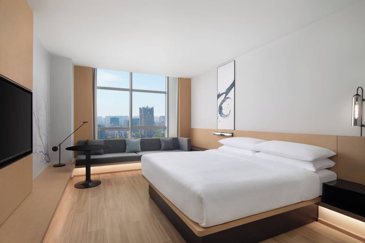 Una habitación de hotel moderna con una cama grande, un sofá, un televisor y vista a la ciudad.