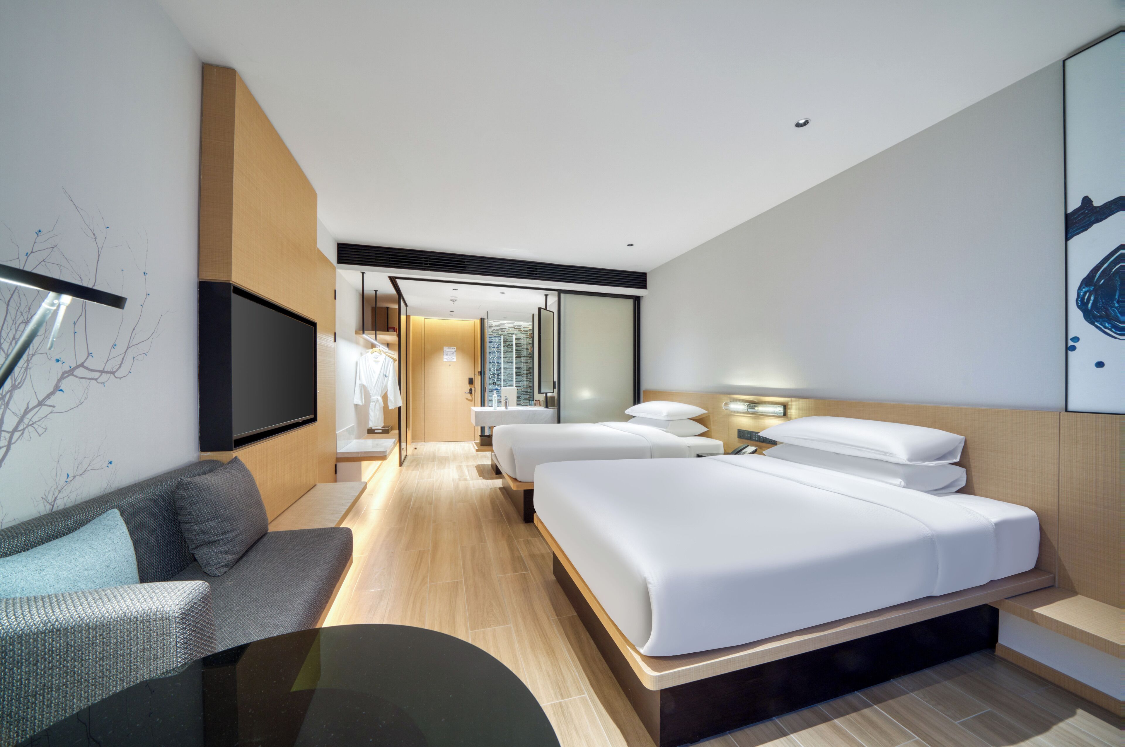 A modern hotel room with a large bed, a sofa, a TV, and a bathroom visible through an open door.