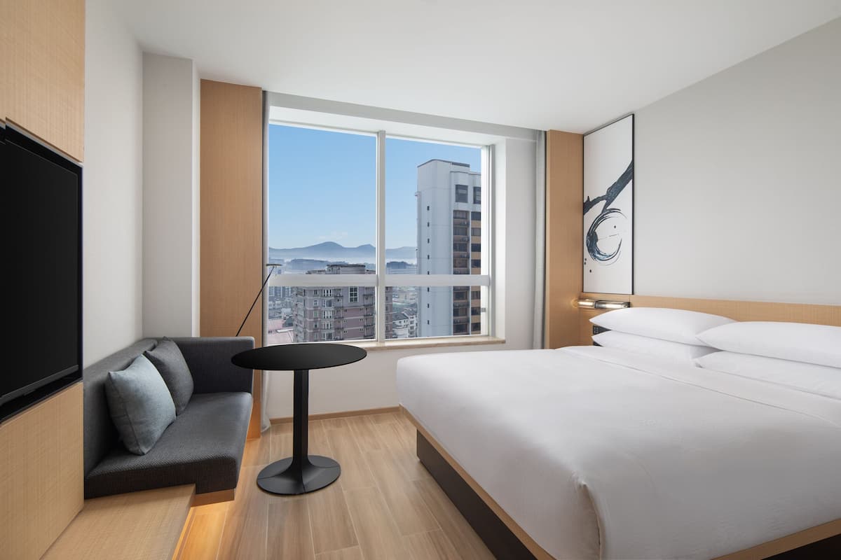 Una habitación de hotel moderna con una cama grande, un sofá, una mesita y un televisor.
