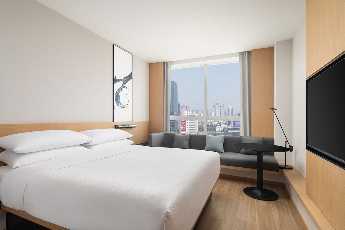 Una habitación de hotel moderna con una cama grande, un sofá, un televisor y vistas a la ciudad.