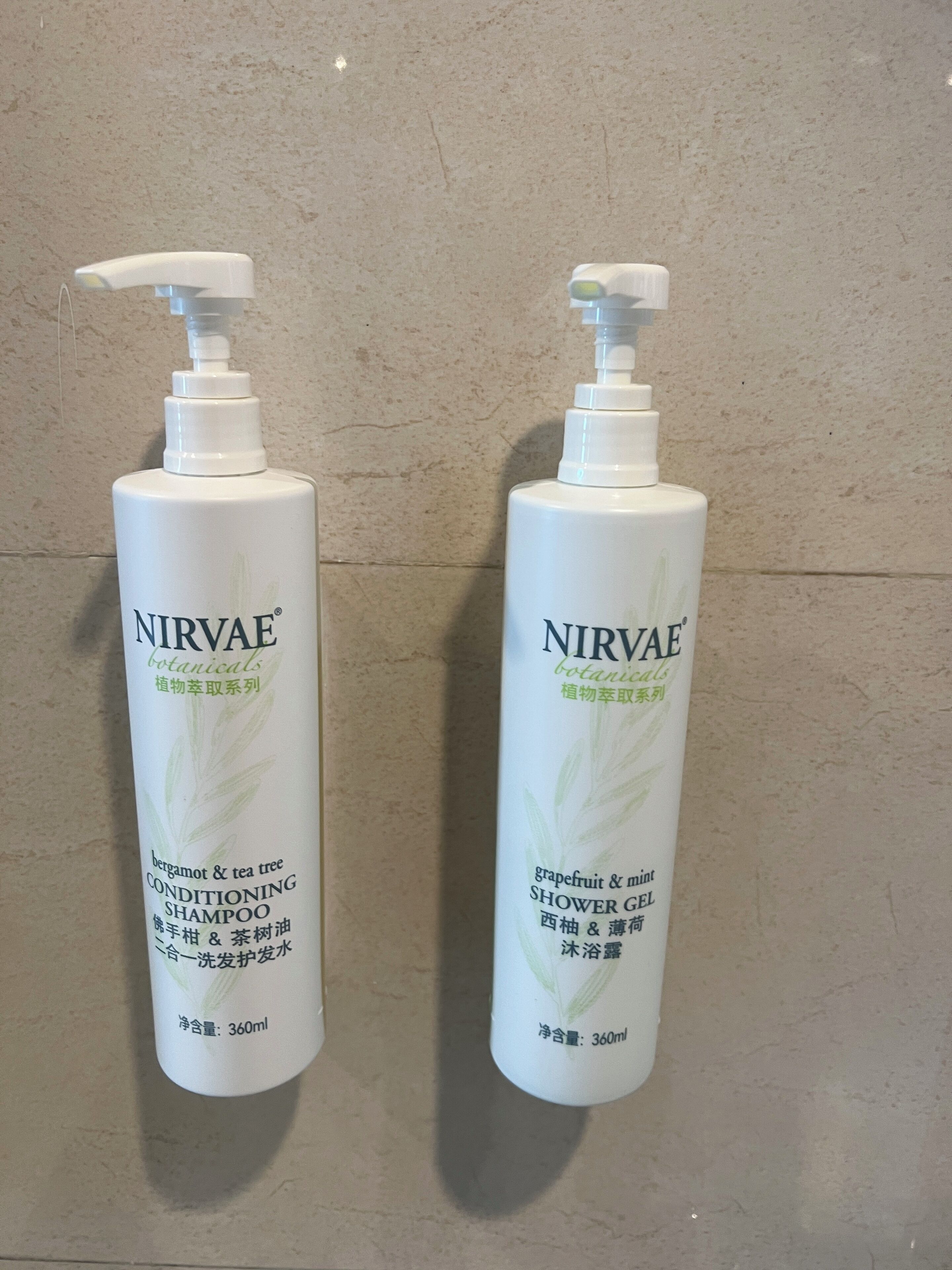 Two bottles of Nirvae botanical shampoo and shower gel on a tiled wall.