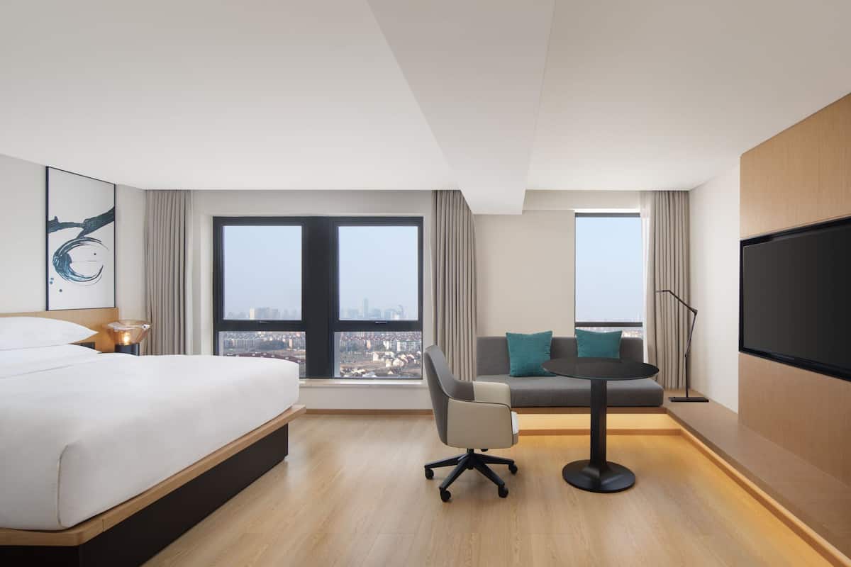 A modern hotel room with a large bed, a sofa, a small table, and a TV.