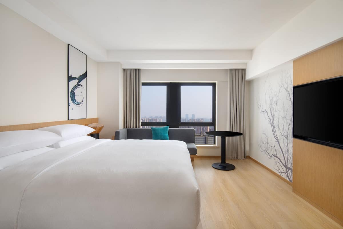 A hotel room with a large bed, a sofa, a TV, and a city view.