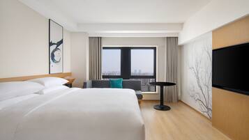 Quarto de hotel com uma cama grande, um sofá, uma TV e vista para a cidade.