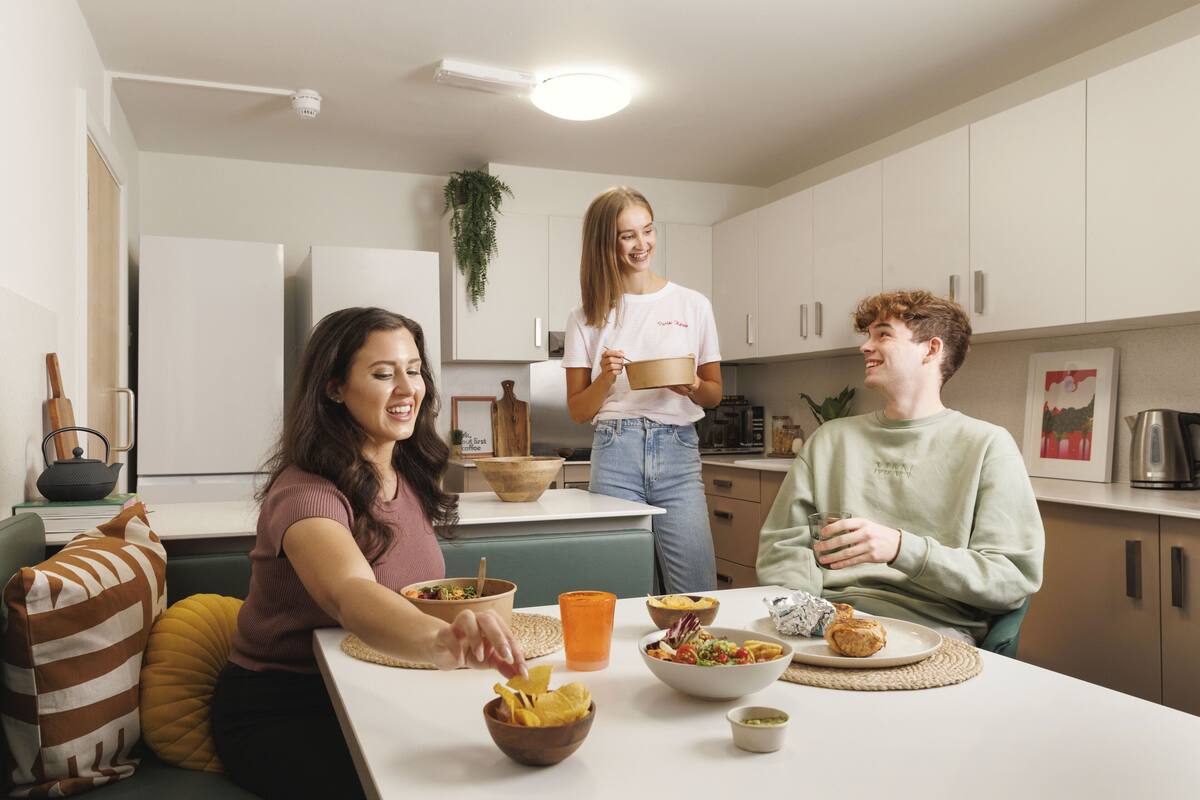 A modern kitchen with white cabinets, a dining table with food, and a person holding a bowl.
