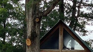 A log cabin with a dormer window, a stone foundation, and a stack of firewood.