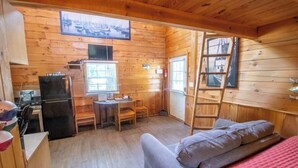 A compact cabin with a kitchenette, a dining area, and a sleeping area with a loft bed.