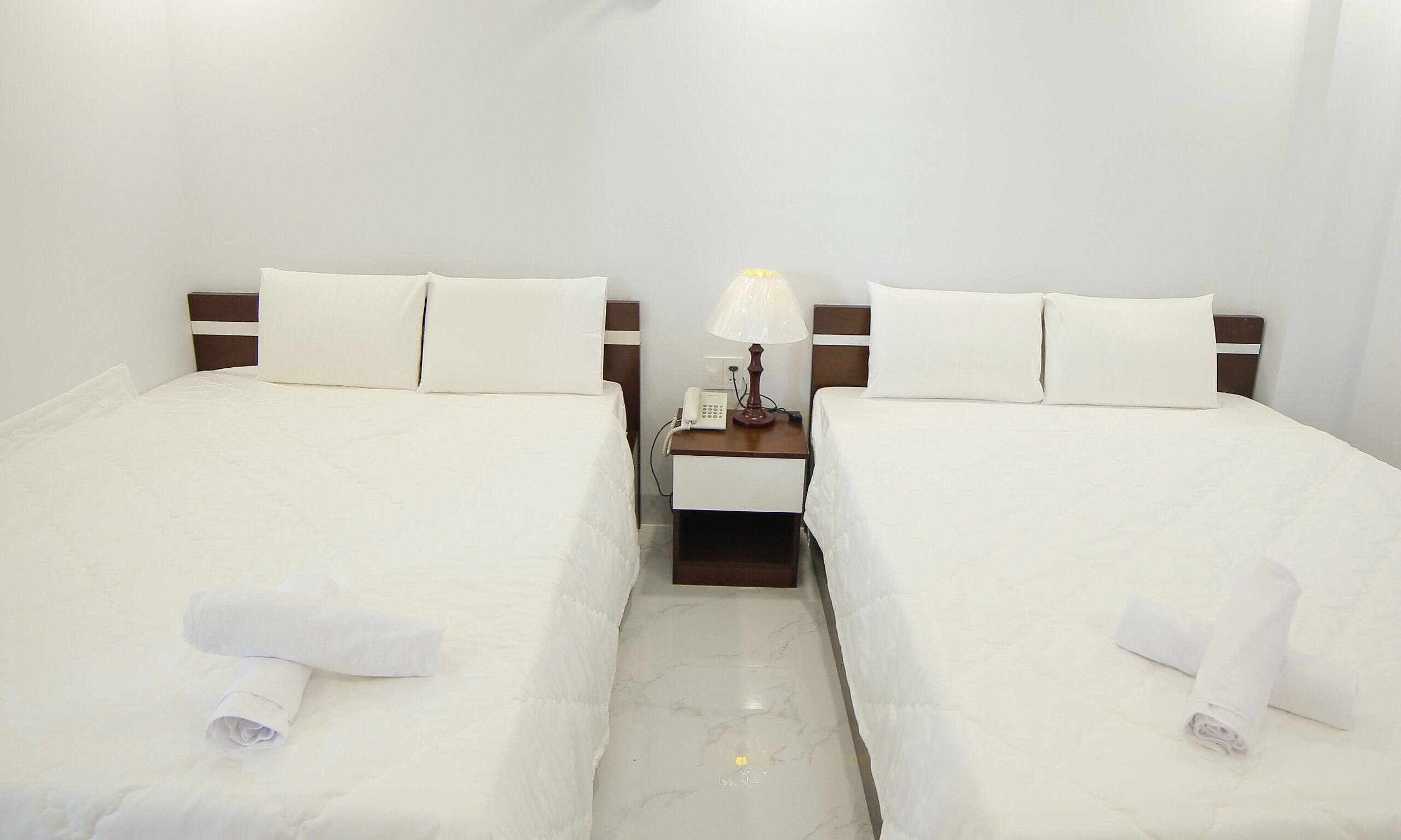 Une chambre d’hôtel avec deux lits, chacun doté de draps et d’oreillers blancs, une table de chevet avec une lampe et un téléphone.