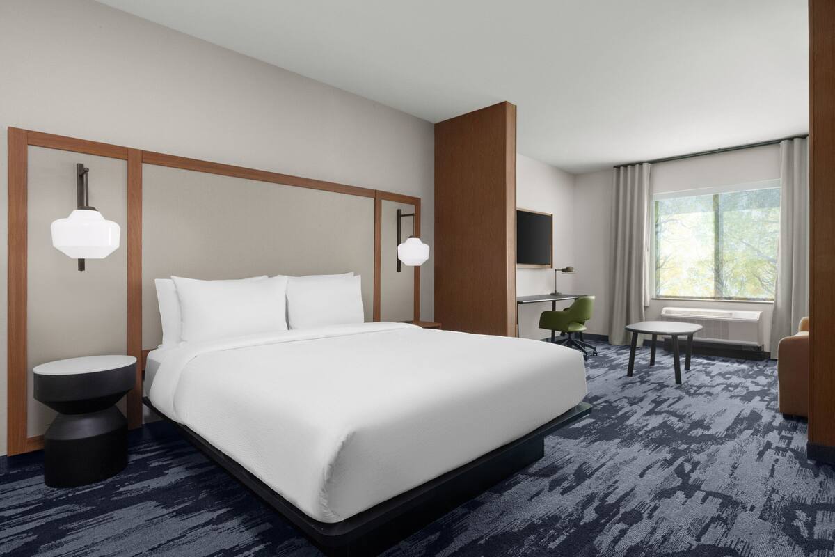 A hotel room with a large bed, two bedside tables, a desk, a chair, and a window with a view of trees.