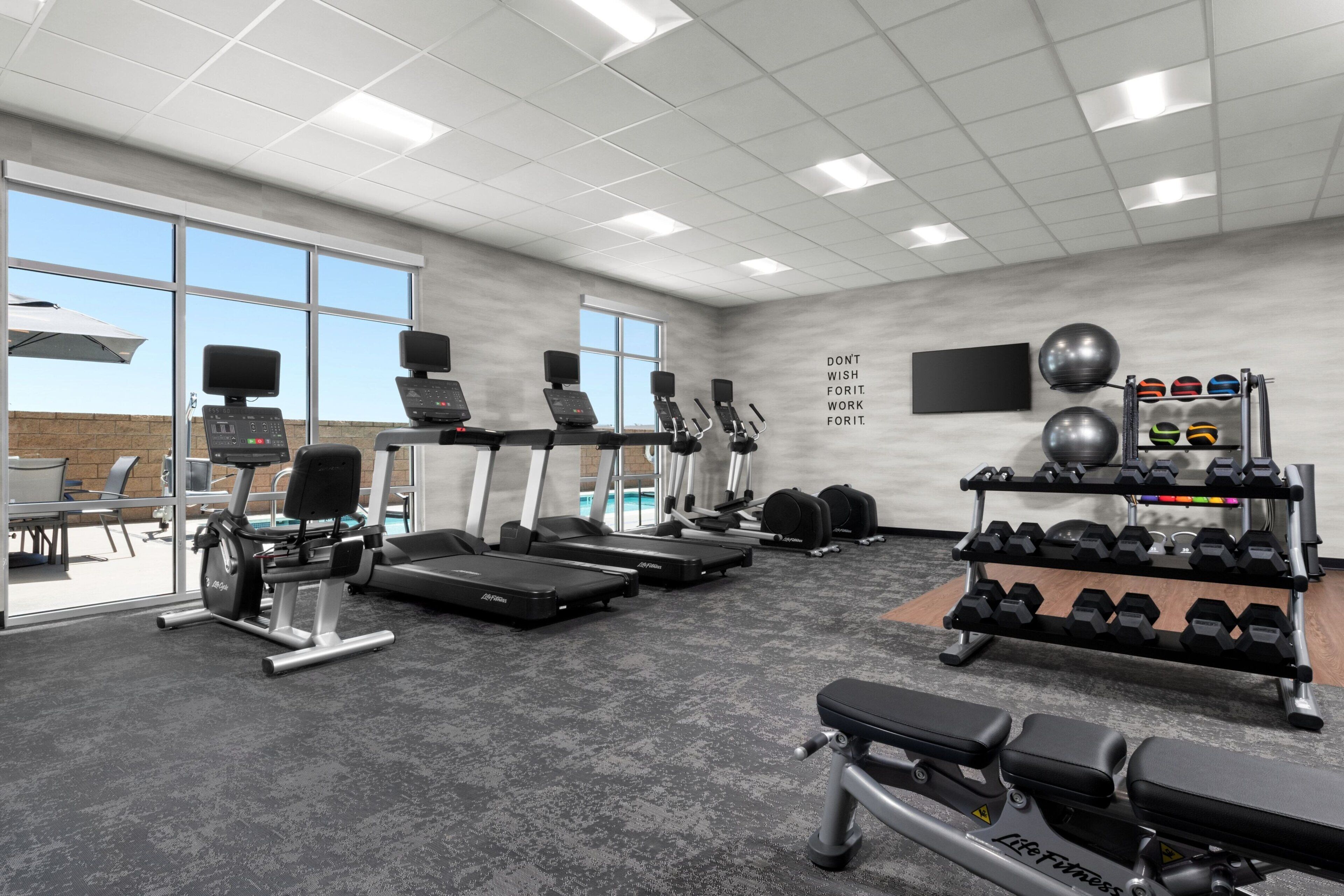 Ein Fitnessraum mit Laufbändern, Crosstrainern, Kurzhanteln und einem motivierenden Zitat an der Wand.