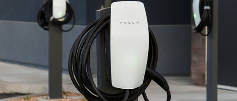 A Tesla charging station with a white charging unit and a black cable.