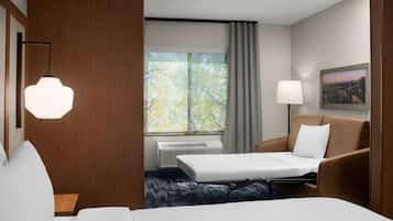 A hotel room with a bed, a sofa, a desk, a lamp, a painting, and a window with curtains.
