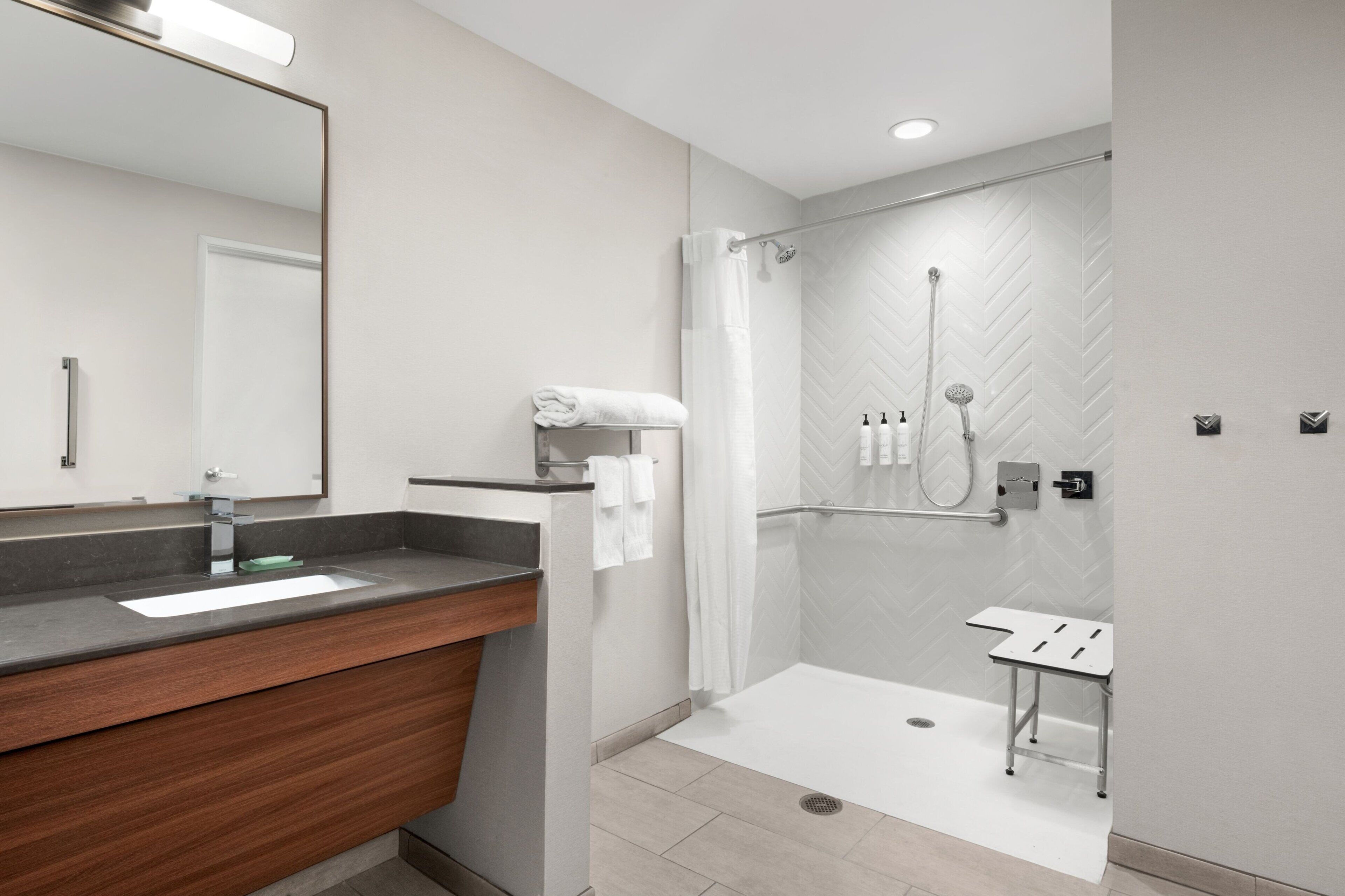 A modern bathroom with a large mirror, a wooden vanity, a shower with a glass door, and a small table.
