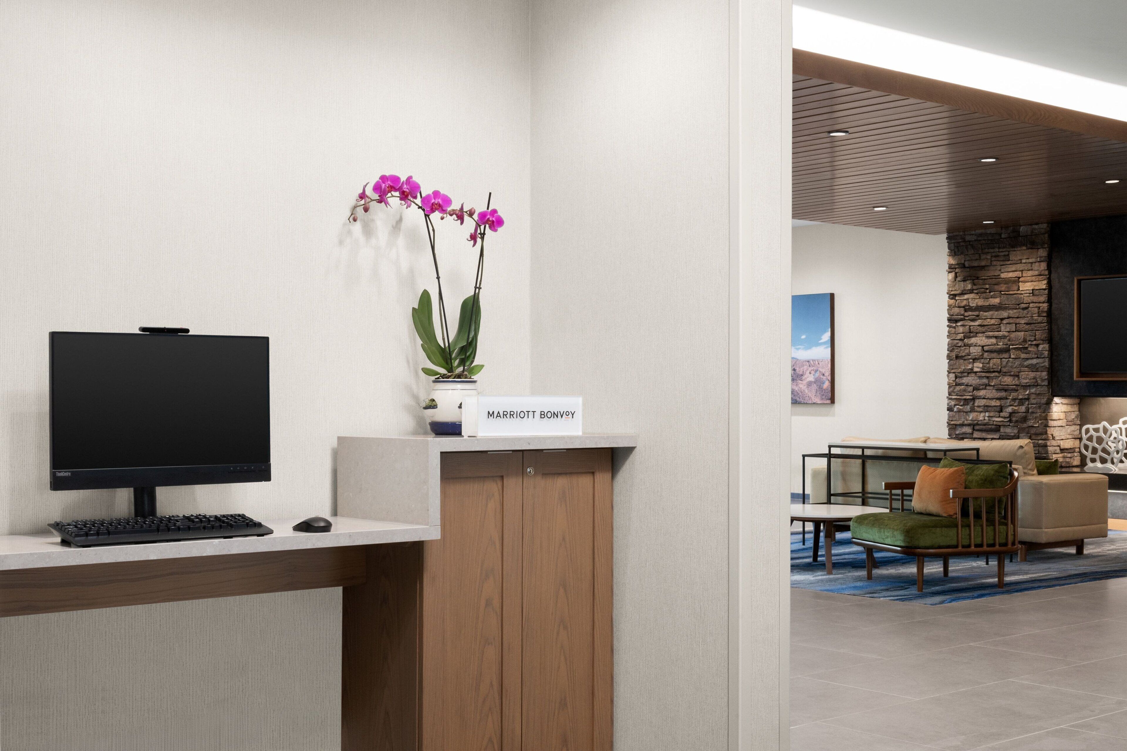 A reception desk with a computer, a vase of orchids, and a sign reading "MARRIOTT BONVOGIO".