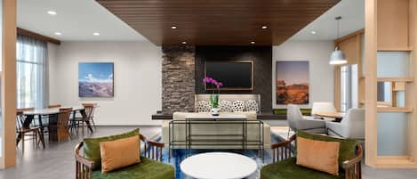 A modern living room with a stone fireplace, green sofas, a round coffee table, and a dining area with wooden chairs.
