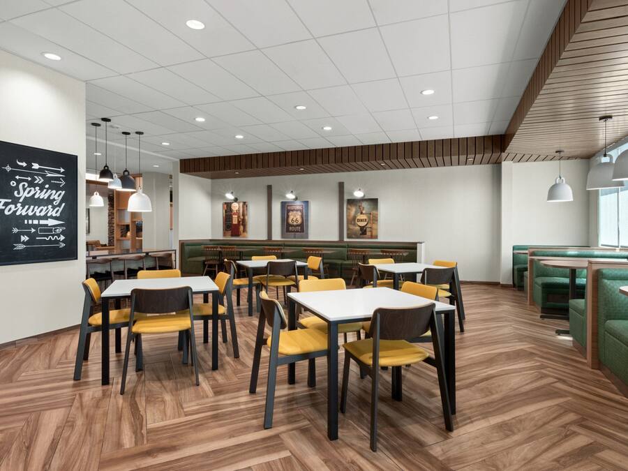 A modern restaurant with wooden flooring, yellow and green seating, and a 'Spring Forward' sign on the wall.