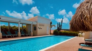 Una piscina con sillones de descanso y una estructura de techo de paja.