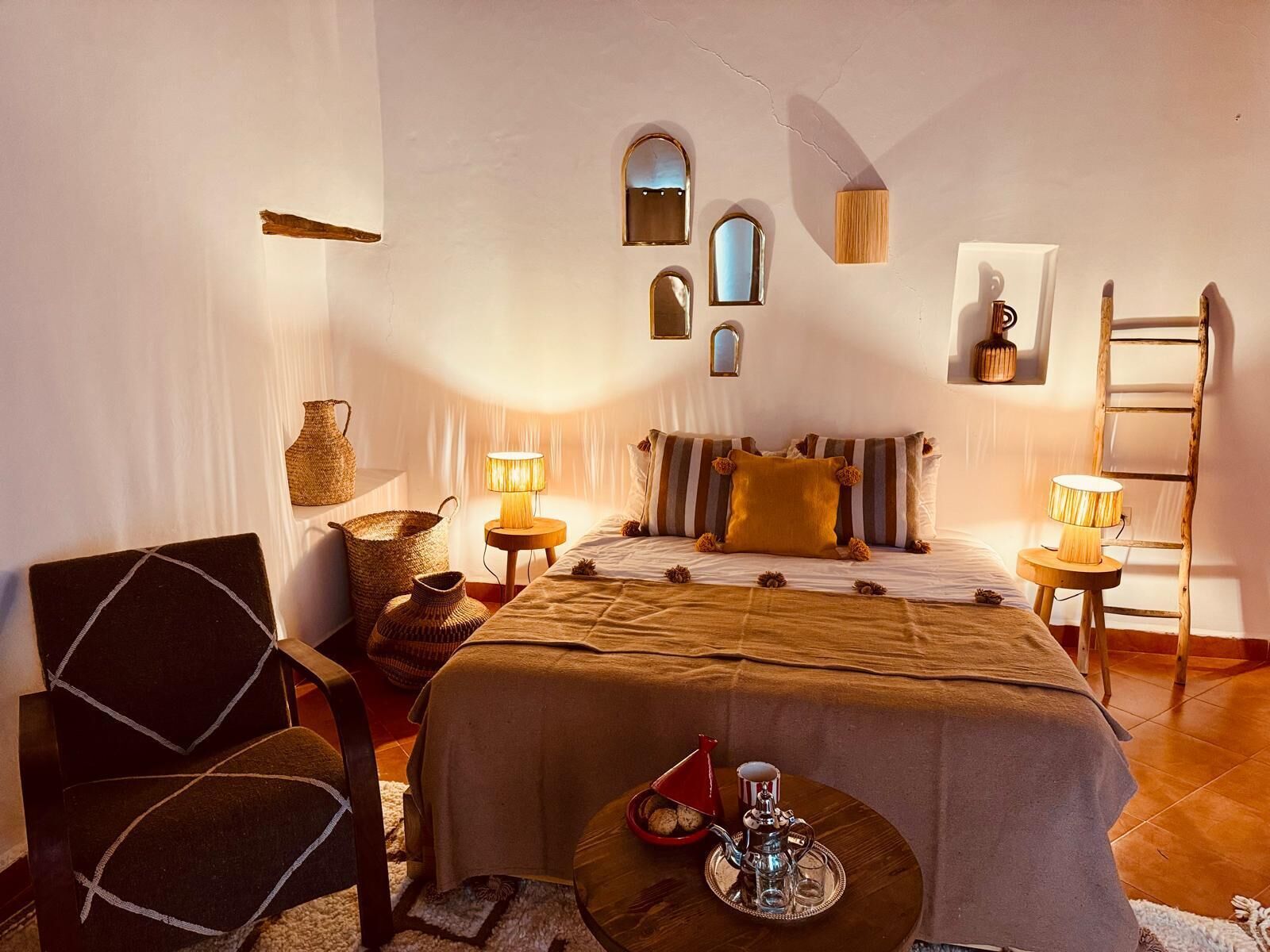A cozy bedroom with a bed, a chair, a small table with a teapot, and a ladder against the wall.