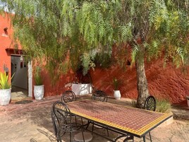 An outdoor patio with a table and chairs, surrounded by potted plants and a red wall.