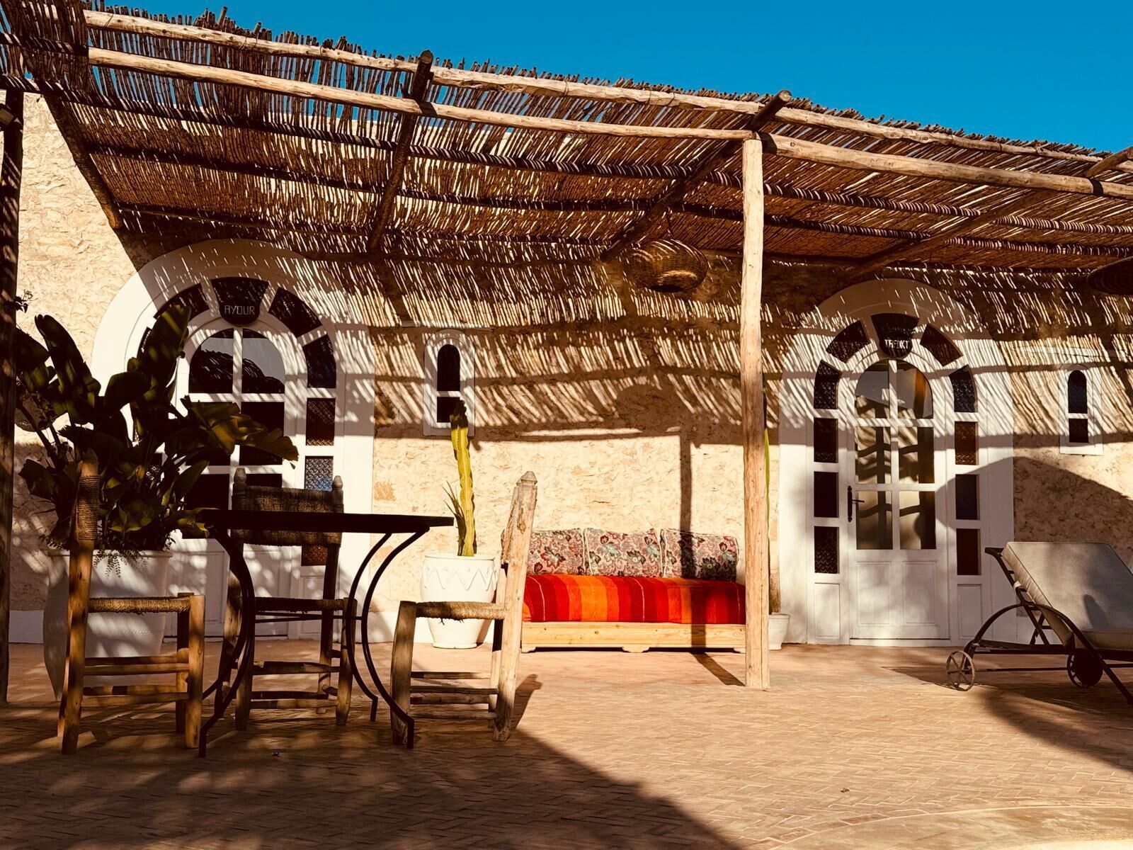 Une terrasse extérieure dotée d’un toit de chaume, de meubles en bois et d’un mur en pierre.