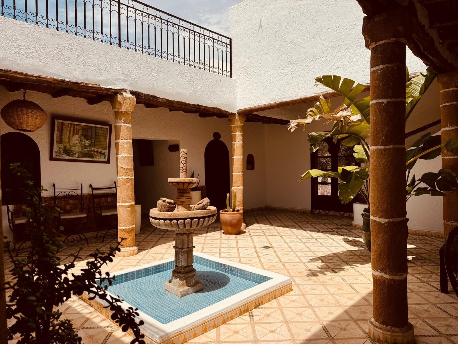 A courtyard with a fountain, tiled floor, and potted plants.