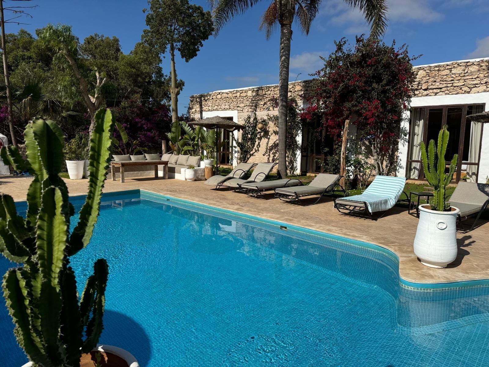 A pool area with lounge chairs, a stone wall, and potted plants.